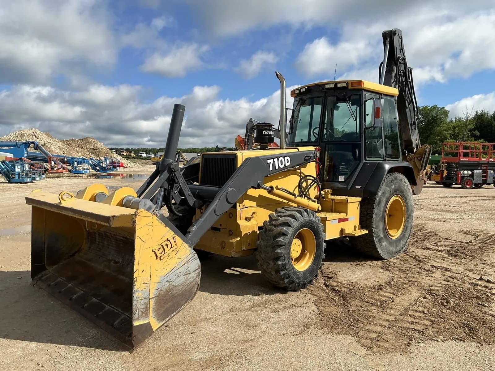 1993 John Deere 710D backhoe loader on a dealer lot — a classic industrial backhoe, front loader bucket down and the hoe folded at the rear