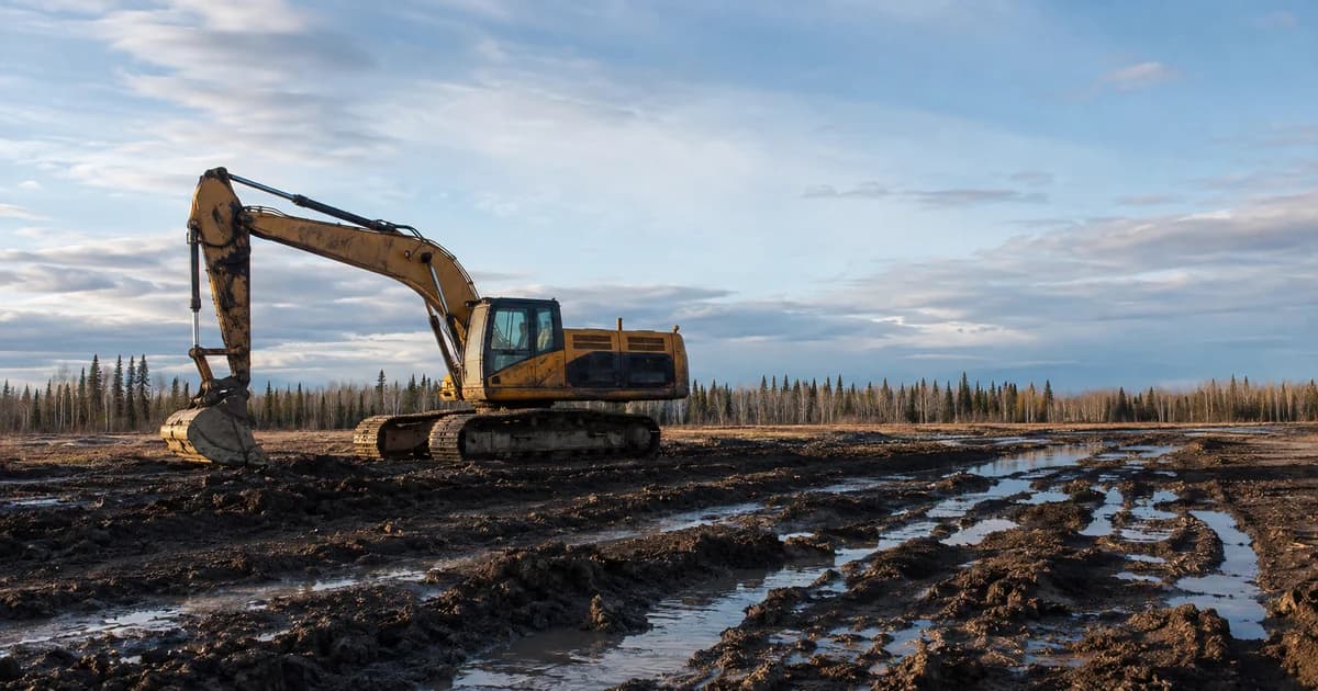 Tracked excavator sitting idle on rutted, water-filled ground during spring breakup in northern Alberta